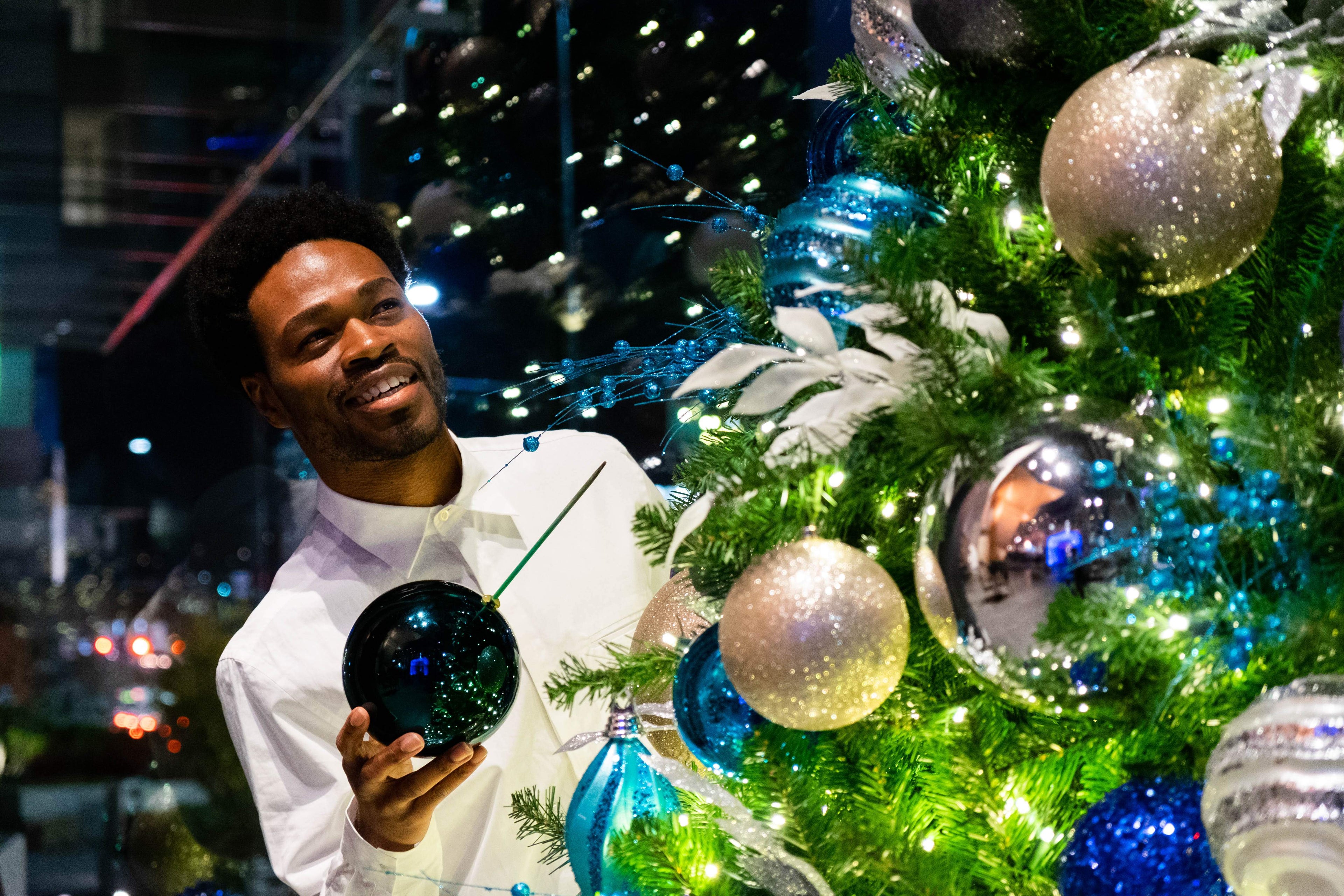 Vance LaRoy a Black American Man holding a Christmas ornament in front of a decorated tree with lights.